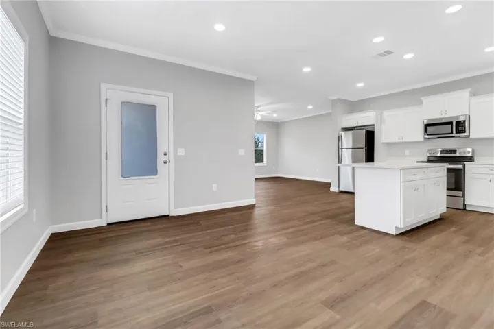 Kitchen featuring crown molding, laminated flooring, with stainless steel appliances, an island, and white cabinetry