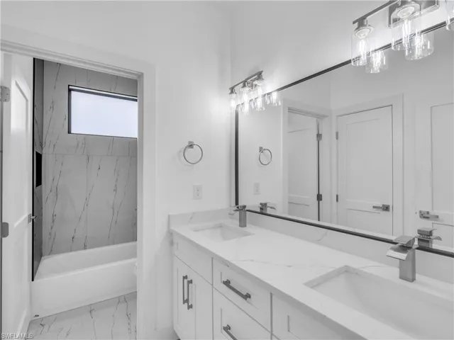 Full bath featuring double vanity, tub / shower combination, and light marble finish flooring