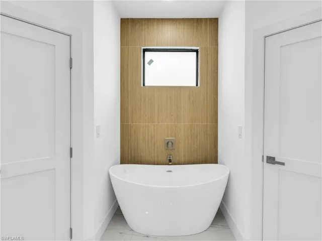 Bathroom with a soaking tub, marble finish floors, and tile walls