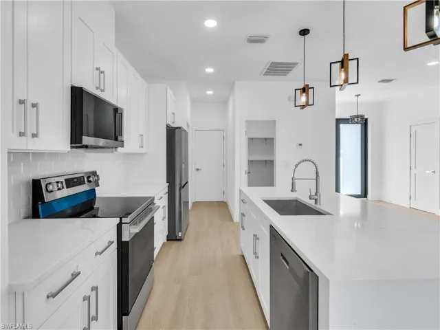 Kitchen featuring stainless steel appliances, white cabinetry, light stone counters, a center island with sink, and light wood finished floors