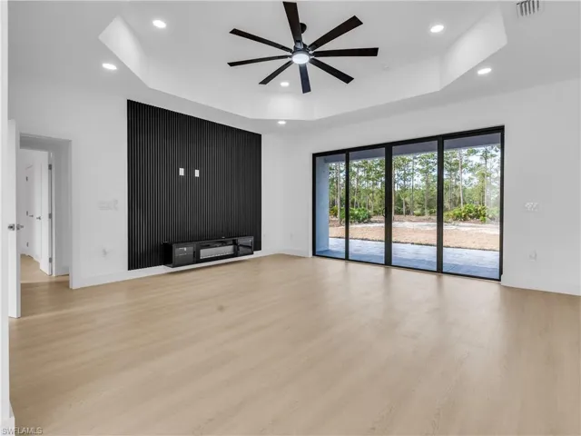Unfurnished living room featuring ceiling fan, light wood-style floors, a tray ceiling, and recessed lighting