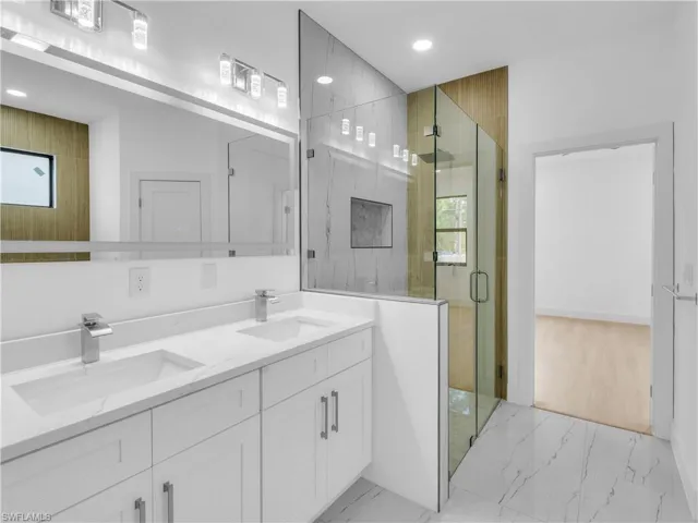 Bathroom featuring a stall shower, double vanity, recessed lighting, and light marble finish flooring