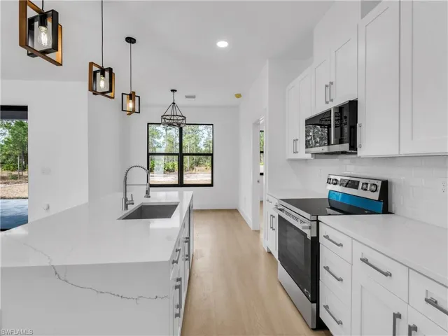 Kitchen featuring stainless steel appliances, white cabinetry, pendant lighting, light stone countertops, and light wood finished floors