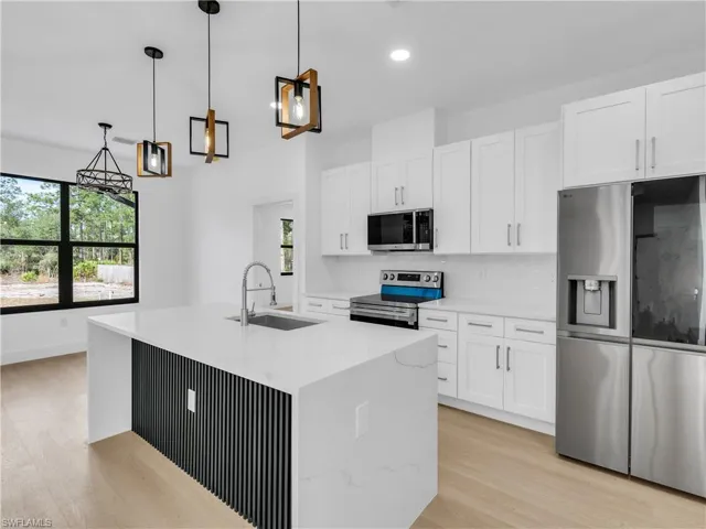 Kitchen featuring stainless steel appliances, pendant lighting, white cabinetry, light wood-style flooring, and light stone countertops