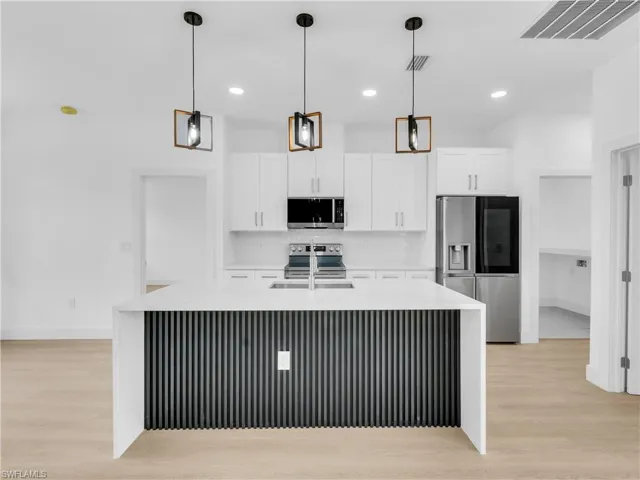 Kitchen featuring light stone countertops, light wood finished floors, stainless steel appliances, and decorative light fixtures