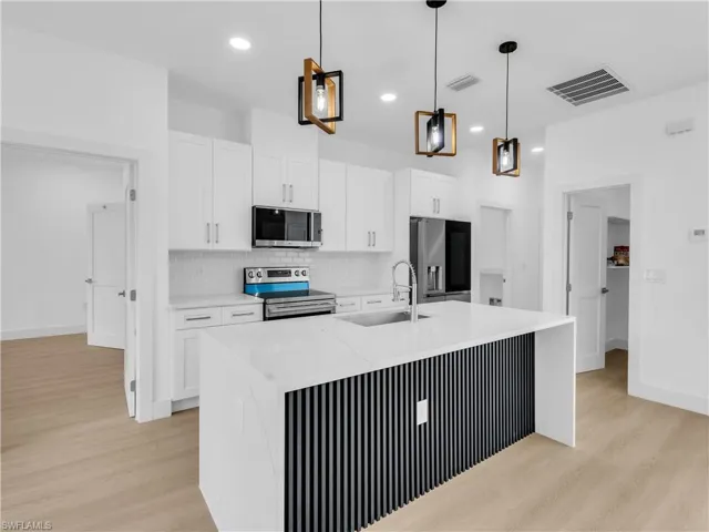 Kitchen featuring light stone countertops, white cabinetry, stainless steel appliances, light wood-type flooring, and pendant lighting
