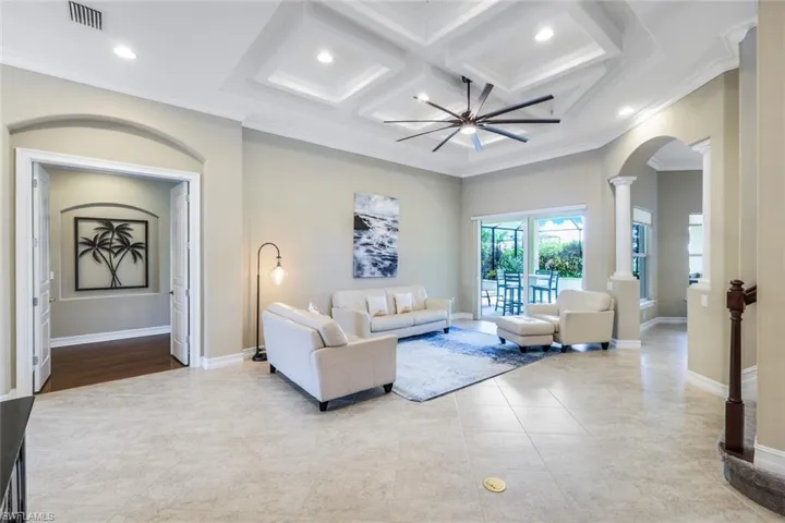 Tiled living area featuring visible vents, crown molding, baseboards, decorative columns, and arched walkways
