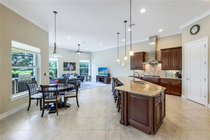 Kitchen featuring decorative backsplash, crown molding, wall chimney exhaust hood, a sink, and open floor plan