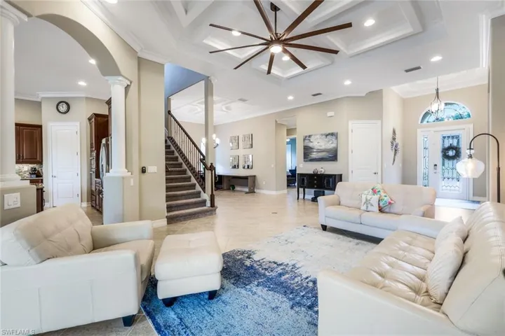 Living area featuring crown molding, coffered ceiling, recessed lighting, ornate columns, and ceiling fan