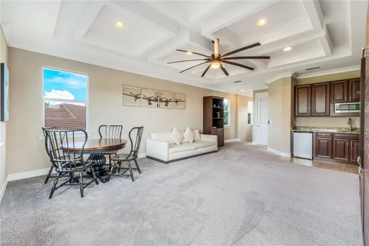Dining area featuring light carpet, indoor wet bar, ornamental molding, and a ceiling fan