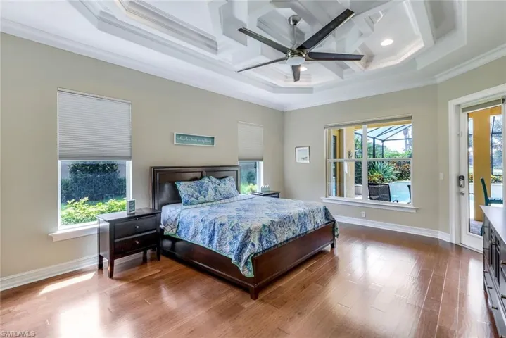 Bedroom with coffered ceiling, ornamental molding, wood finished floors, and multiple windows