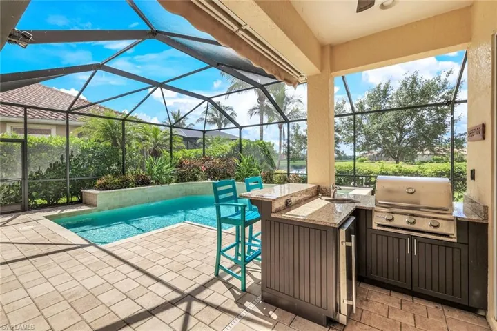 Pool with area for grilling, a patio, glass enclosure, outdoor dry bar, and a grill