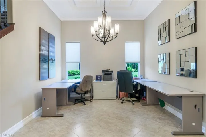 Office with baseboards, an inviting chandelier, crown molding, and a raised ceiling