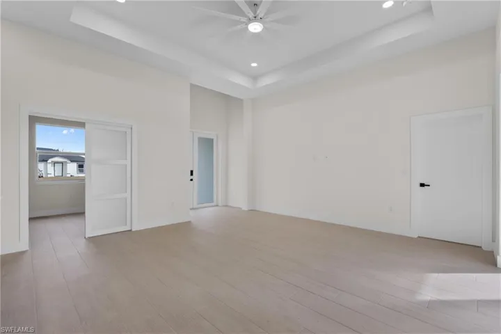 Unfurnished bedroom featuring a tray ceiling, light wood-style flooring, a towering ceiling, recessed lighting, and ceiling fan