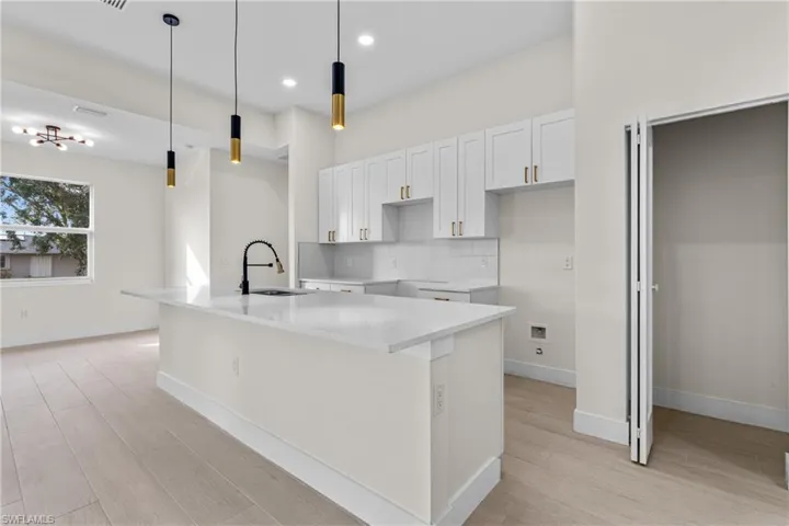 Kitchen featuring light stone countertops, white cabinets, a center island with sink, decorative light fixtures, and tasteful backsplash