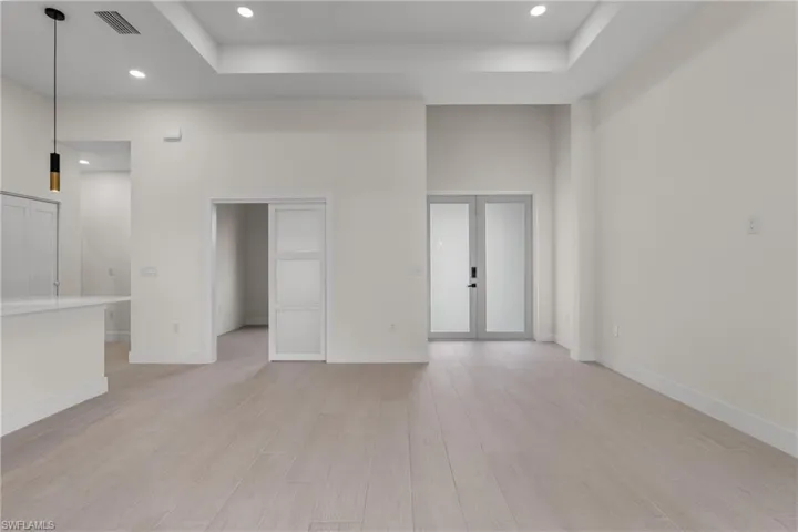 Unfurnished living room with recessed lighting, light wood finished floors, a tray ceiling, a high ceiling, and french doors