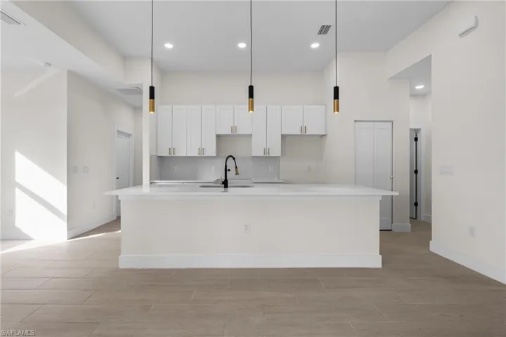 Kitchen with light stone counters, recessed lighting, pendant lighting, a kitchen island with sink, and white cabinets