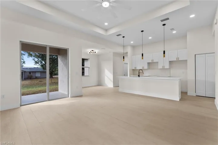 Unfurnished living room with a tray ceiling, recessed lighting, ceiling fan, a high ceiling, and light wood-style floors