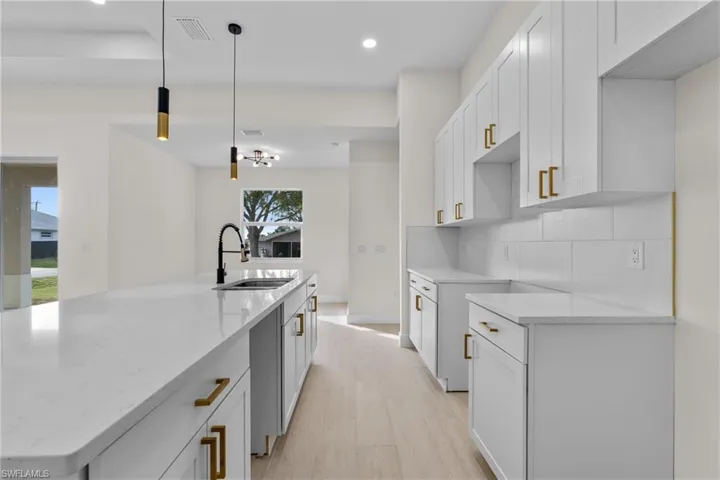 Kitchen featuring white cabinetry, light stone countertops, recessed lighting, hanging light fixtures, and a center island with sink