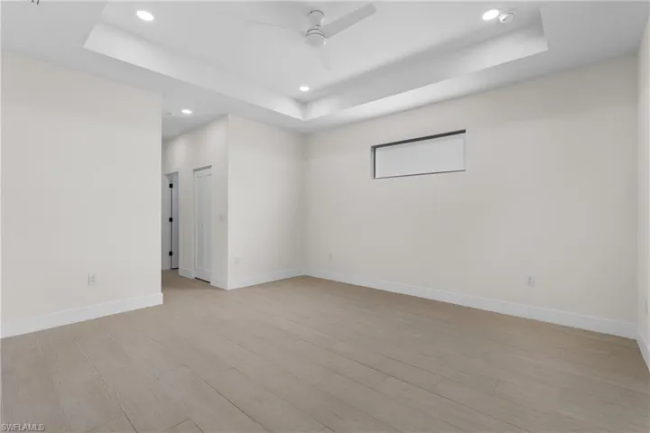 Empty room featuring a raised ceiling, light wood-type flooring, recessed lighting, and ceiling fan