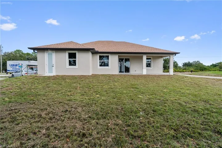 Rear view of property with stucco siding, a yard, and roof with shingles