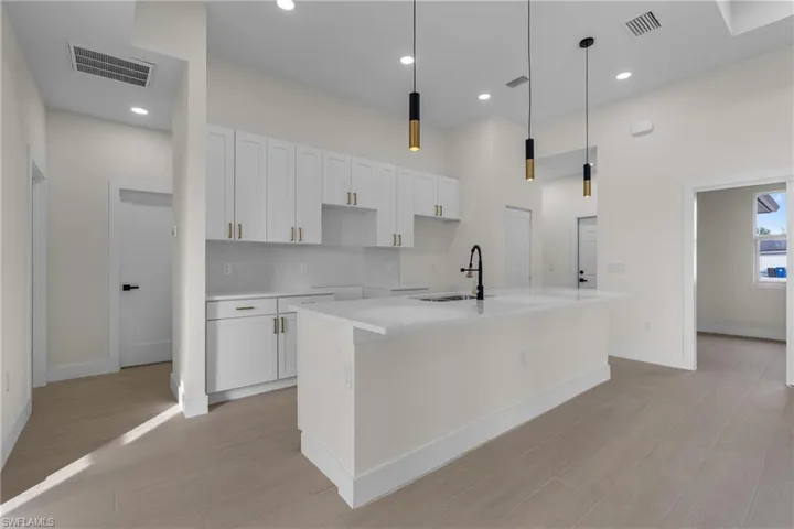 Kitchen with a center island with sink, light stone countertops, hanging light fixtures, white cabinets, and recessed lighting