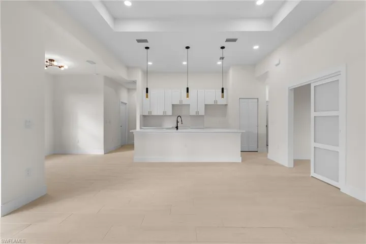 Kitchen with a center island with sink, white cabinets, recessed lighting, decorative light fixtures, and a raised ceiling