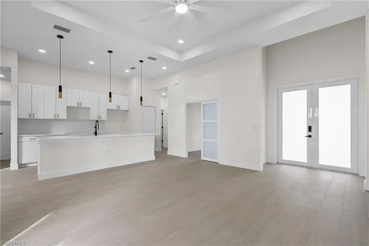 Unfurnished living room with a high ceiling, a raised ceiling, recessed lighting, light wood-style flooring, and french doors