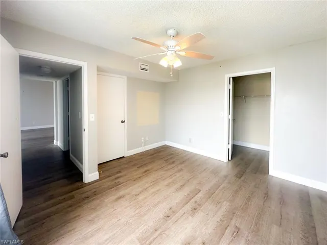 Unfurnished bedroom featuring a spacious closet, a textured ceiling, light wood-style flooring, and a ceiling fan