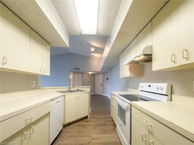 Kitchen with white appliances, under cabinet range hood, light wood-style flooring, light countertops, and lofted ceiling