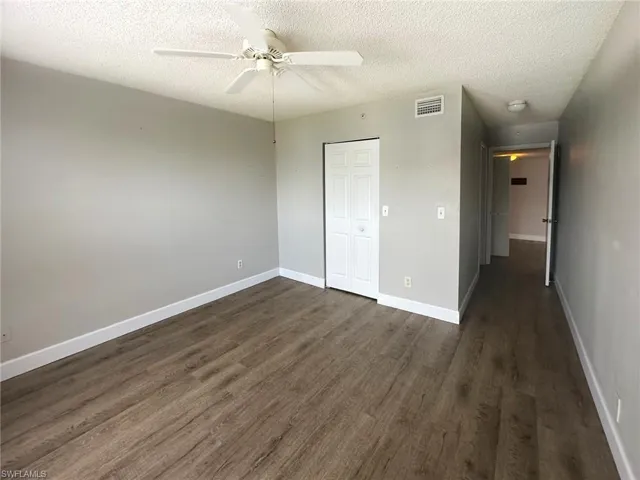 Unfurnished bedroom featuring a textured ceiling, dark wood-type flooring, ceiling fan, and a closet