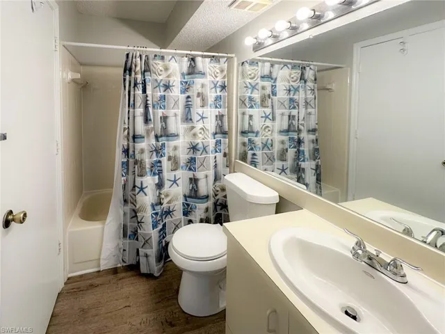 Bathroom featuring shower / bath combo with shower curtain, dark wood-style floors, vanity, and a textured ceiling