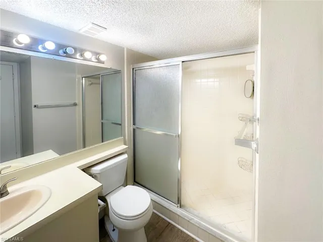 Full bathroom with vanity, a shower stall, a textured ceiling, and wood finished floors