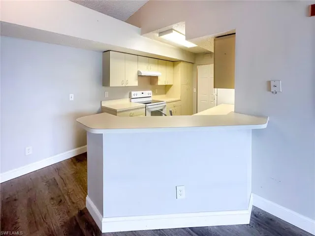 Kitchen with light countertops, a peninsula, white electric range, dark wood-style flooring, and under cabinet range hood