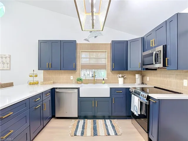 Kitchen featuring blue cabinetry with gold-finish hardware, white countertops, stainless steel appliances, and a farmhouse sink