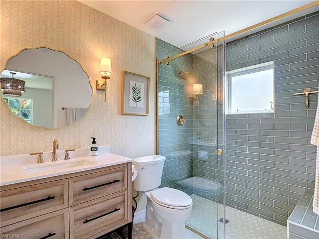 Bathroom featuring a wood-finish vanity with a white countertop, gold-tone fixtures, and a frameless glass shower enclosure