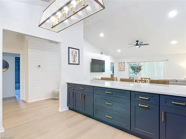 Spacious open-concept interior featuring light wood-finish flooring, vaulted ceilings with recessed lighting, and a contemporary ceiling fan