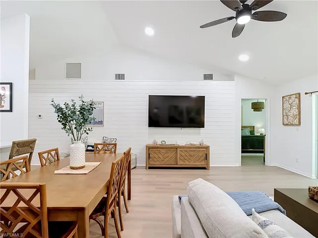 Vaulted ceilings, recessed lighting, wood-finish flooring, white shiplap accent wall, and a ceiling fan with integrated lighting