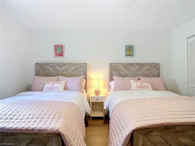 Two wood-finish bed frames with chevron headboards, light wood-finish flooring, white walls, and a louvered bi-fold closet door