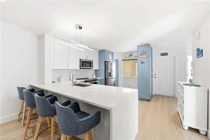 Kitchen featuring a peninsula, light wood finished floors, a kitchen breakfast bar, stainless steel appliances, and light stone countertops