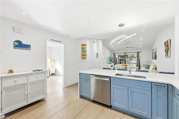 Kitchen featuring blue cabinetry, lofted ceiling, stainless steel dishwasher, light stone countertops, and open floor plan