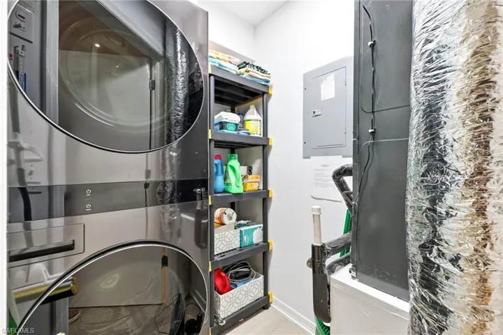 Laundry room featuring electric panel, estacked washer and dryer, and heating unit