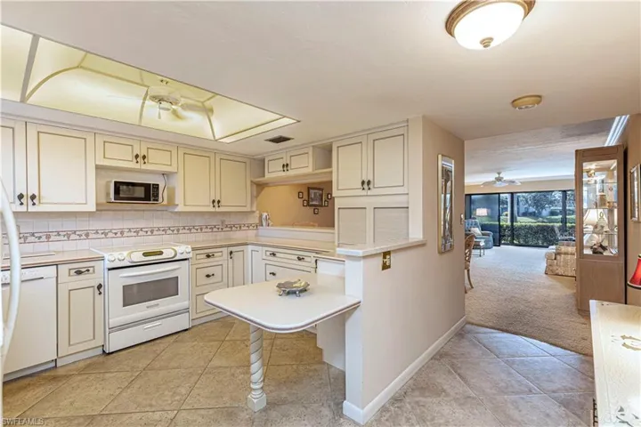 Light-Bright Kitchen with light tile patterned flooring, cream cabinets, white appliances, tasteful backsplash,