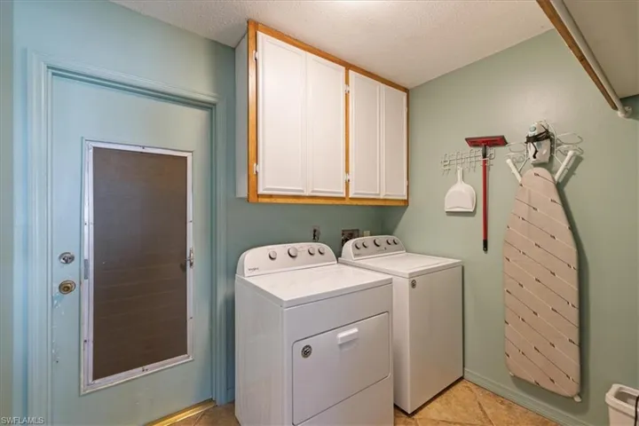 Laundry room featuring cabinet space, washer and clothes dryer, a textured ceiling, and light tile patterned floors