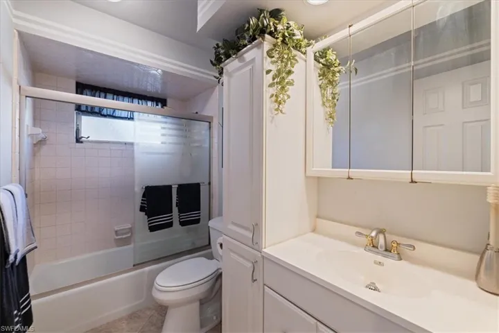 Full bathroom featuring vanity, toilet, combined bath / shower with glass door, and tile patterned floors