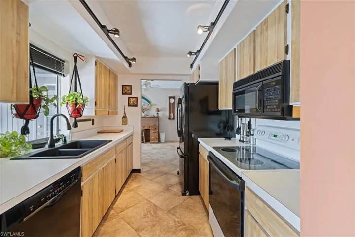 Kitchen with black appliances, a sink, light countertops, and light brown cabinets