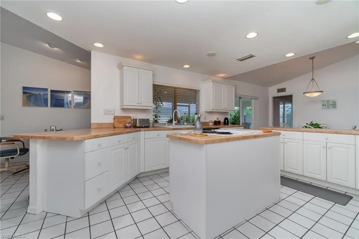 Kitchen with lofted ceiling, sink, hanging light fixtures, white cabinets, and kitchen peninsula