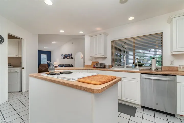 Kitchen with light tile patterned flooring, washer / dryer, sink, stainless steel dishwasher, and white cabinets