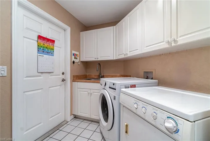 Laundry room featuring separate washer and dryer, sink, light tile patterned floors, and cabinets