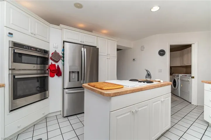 Kitchen with a kitchen island, stainless steel appliances, white cabinets, light tile patterned flooring, and separate washer and dryer